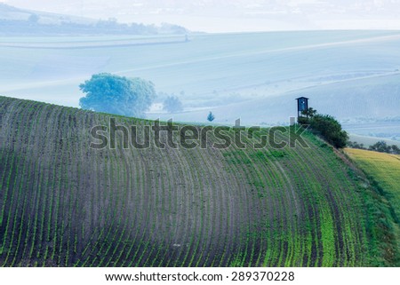Rural Europe background - Moravian rolling landscape with hunting tower shack in early morning on sunrise. Moravia, Czech Republic