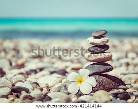 Zen meditation spa relaxation background - vintage retro effect filtered hipster style image of   balanced stones stack with frangipani plumeria flower close up on sea beach