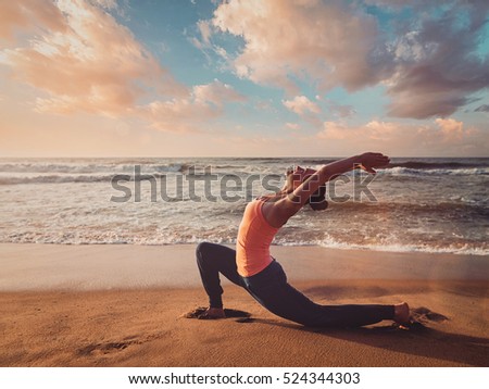 Vintage retro effect filtered hipster style image of Yoga outdoors - sporty fit woman practices yoga Anjaneyasana - low crescent lunge pose outdoors at beach on sunset