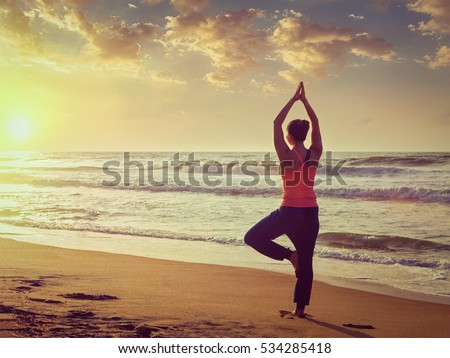 Vintage retro effect filtered hipster style image of Yoga outdoors - sporty fit woman doing Hatha yoga asana Vrikshasana tre pose on tropical beach on sunset