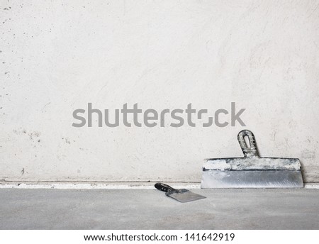 Masonry trowels near a grey plaster wall
