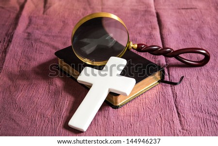 A bible, cross and magnifying glass. The cross is reflected in the glass of the magnifying glass.