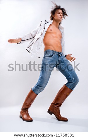 Fashion shot of a Young Man a trendy european man dressed in contemporary cloth. Man in a white shirt, jeans and boots. Denuded torso