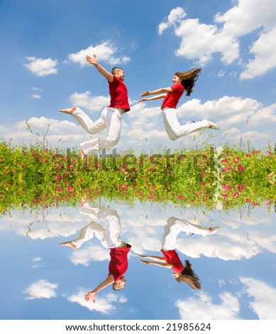 Happy Young Couple - team is jumping in the sky above a green meadow. Reflected in water