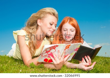 Two beautiful girls with notebooks outdoors. Lay on the green grass.