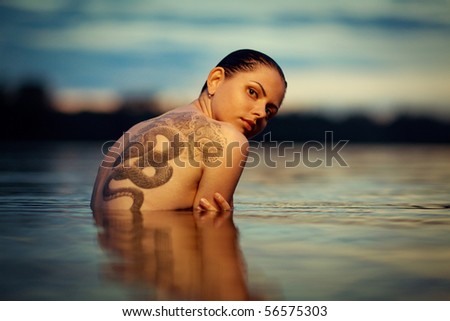 Young tattooing girl swiming in sea waves. An art photo. A beautiful landscape.