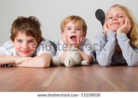 Three kids are lying on their bellies on the floor