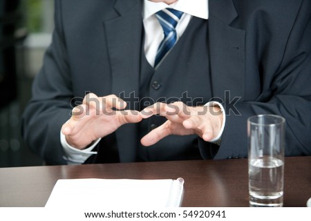 cutout af a male torso in a three-parted gray suit with his hands gesticulating over the desk