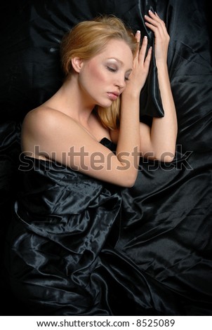 Beautiful woman resting with eyes closed in bed under black satin sheets