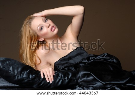 Beautiful woman relaxing under black satin sheets