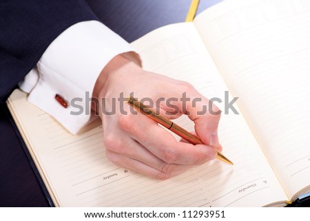 The businessman in a suit behind a table, with a ball pen in hands.