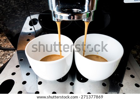 Two cups of coffee that goes down from machine coffee bar