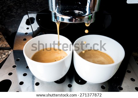 Two cups of coffee that goes down from machine coffee bar