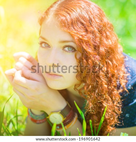 Beautiful redhead girl lay on grass. Soft focus on eyes. With green highlights on the face.