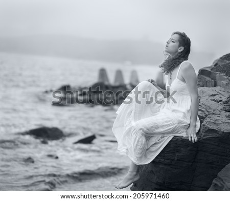 Woman sitting on the coast on beach and looks into the distance at sea. Selective soft focus. Black and white image.