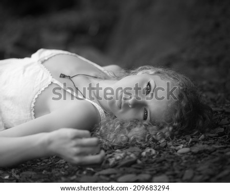 Beautiful woman at the rocky beach in a white dress laid down on the gravel. Black and white.