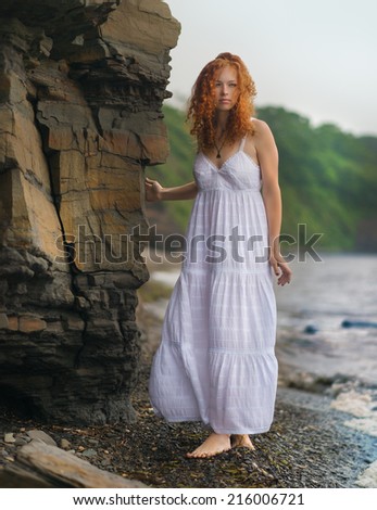Beautiful redhead woman goes along the coast.