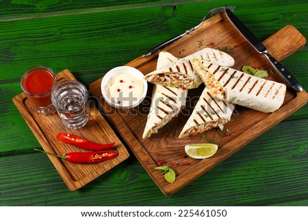 Enchiladas with lime and sauce, glass of tequila and tomato juice with jalapeno pepper on wooden board