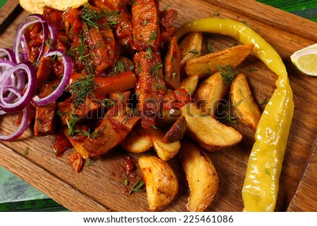 Mexican cuisine meat pieces in sauce with fried potato, onion rings, chips and jalapeno pepper on wooden board closeup