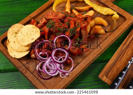 Mexican cuisine meat pieces in sauce with fried potato, onion rings, chips and jalapeno pepper on wooden board