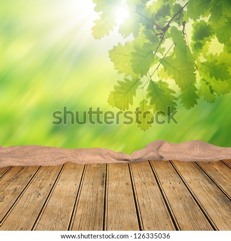Wooden empty table with natural green background and oak leaves. Great for products advertisements.