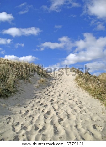 sand dune with footprints under a deep blue sky with some white clouds