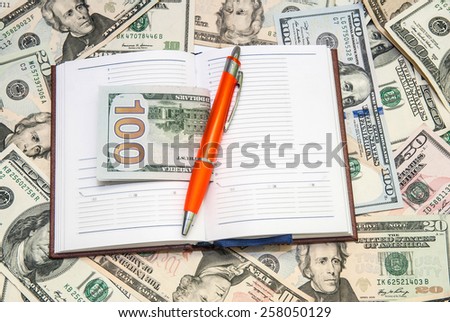 pen lying  on open notebook with dollars background