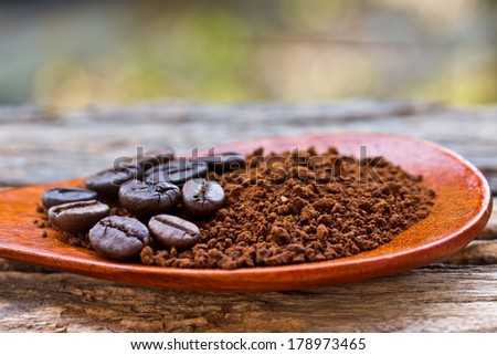 Roasted coffee beans and ground coffee in wooden spoon on textured wood.