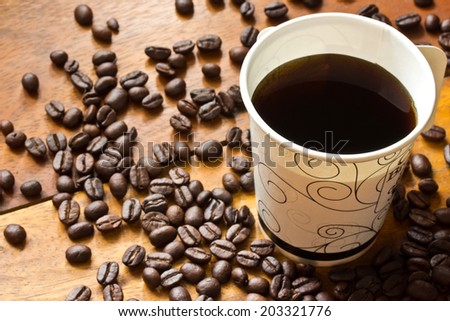 a paper cup of black coffee and coffee beans on wooden table