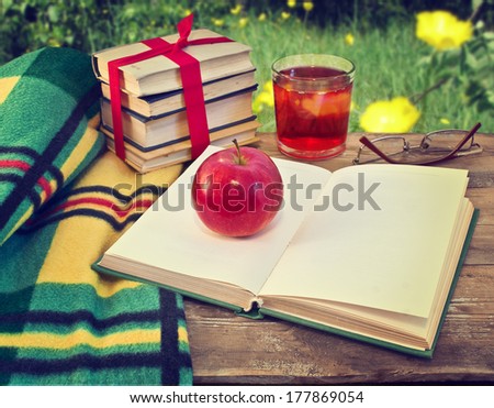 Open book on table in garden. Still life with books and apple