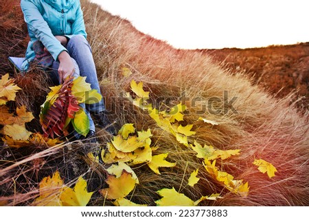 Woman sitting on the grass with a bouquet of autumn leaves. Autumn Landscape. Toning effect. Instagram