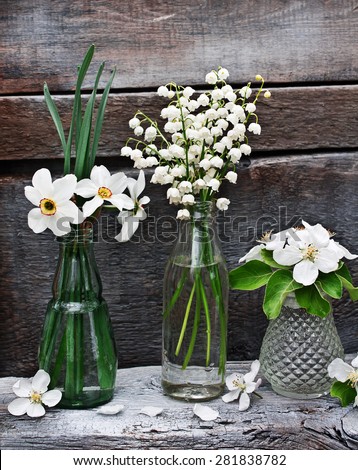 Small vases and bottles with spring flowers and flowering branches of apple on the old wooden background