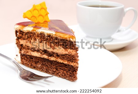 Piece of honey cake on plate with fork and tea cup