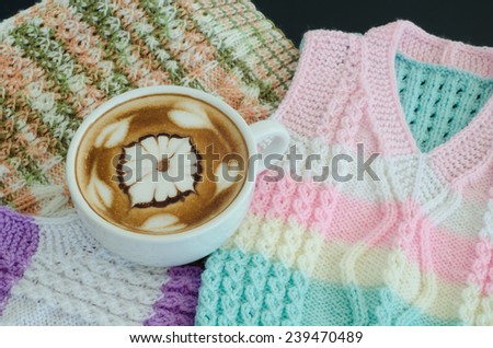 A cup of latte art on a knitted vest background