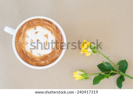 A cup of coffee with latte art and yellow rose on brown paper background