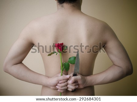 Picture a man holding a red rose and knife behind his back