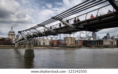 LONDON-MAY 28 :People walking across a footbridge Millennium Bridge. Background is St Paul\'s cathedral in London. Bridge was opened 10 June 2000. View on May 28, 2012