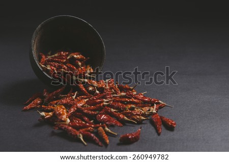 Dried red chillies spilled from a old wooden bowl on a dark background.