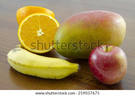 Combination of fruit over a wooden table: sliced orange, mango, apple and banana