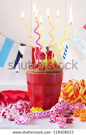 A birthday cupcake with spaghetti candles. Ribbons and garland for the party feeling.