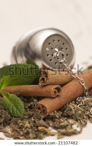 fresh tea leaves with cinnamon sticks, mint and a tea ball