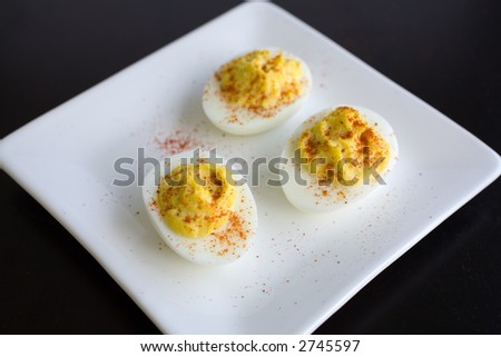Three deviled eggs with smoked paprika on a white plate