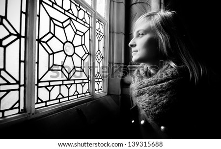 Young teenager watching throw the glazed shiny window