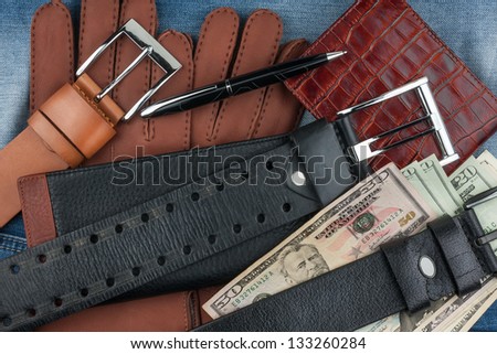Pen, gloves, purses, belts and money on jeans background