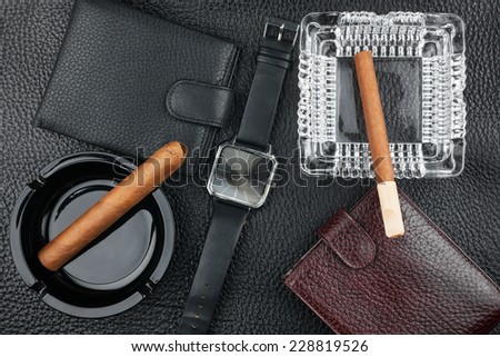 Two ashtray with cigars, two purses and watches on the natural leather, luxury background