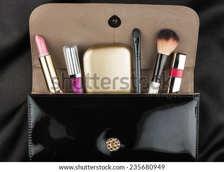 Black patent leather bag  with cosmetics, on black background