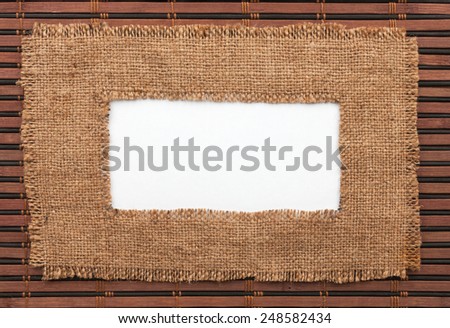 Frame made of burlap with white background lying on a bamboo mat, with space for your text