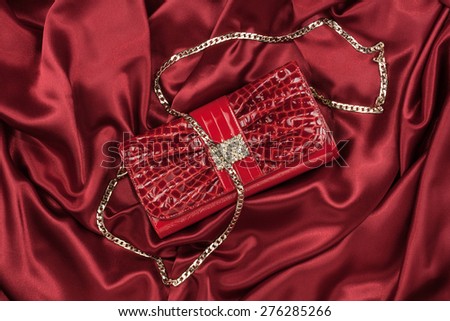 Red lacquer bag lying on a red silk, as background