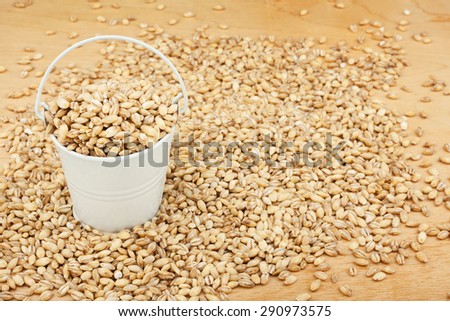 White bucket with pearl barley on the wooden floor, as a background