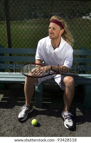 A blonde male tennis player waits his turn on the sideline bench